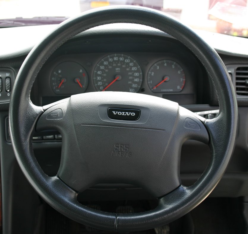 Photograph looking down at a driver's hands on a Volvo steering wheel.